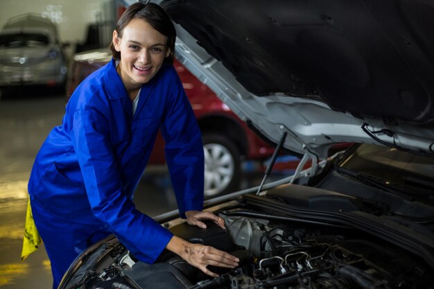 Mecánico de sexo femenino que sonríe mientras que el examen de un coche