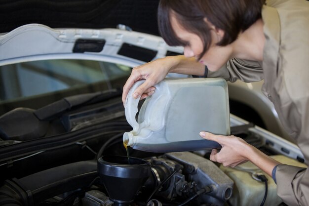 Mecánico de sexo femenino que vierte aceite lubricante en el motor de un coche