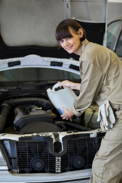 Foto gratuita mecánico de sexo femenino que vierte aceite lubricante en el motor de un coche