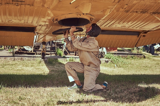 Foto gratuita mecánico en uniforme y casco volador repara un avión militar retro en un museo al aire libre.