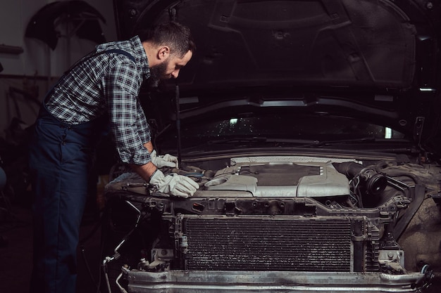 Foto gratuita mecánico en uniforme reparando auto en el garaje. estación de servicio.