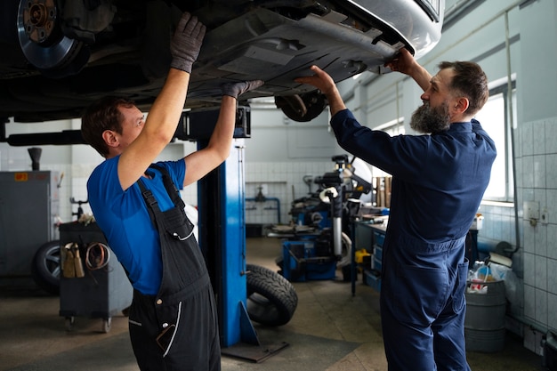 Foto gratuita mecánicos masculinos trabajando juntos en el automóvil en la tienda