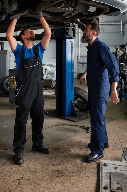 Foto gratuita mecánicos masculinos trabajando juntos en el automóvil en la tienda