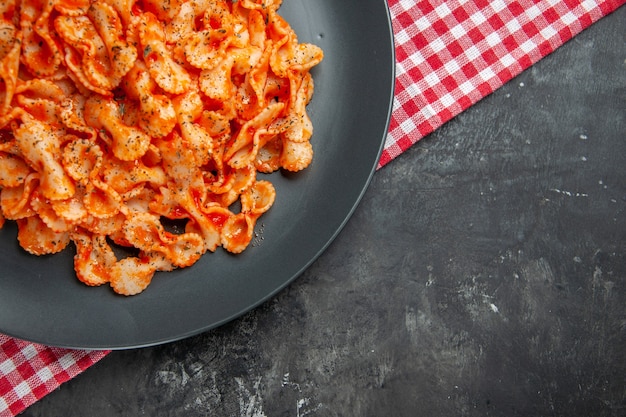 Media foto de deliciosa pasta en una placa negra para cenar sobre una toalla despojada de rojo sobre fondo oscuro