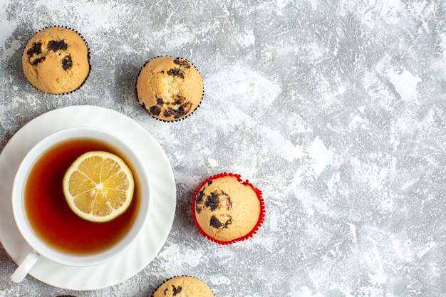 Media foto de deliciosos cupcakes pequeños con chocolate alrededor de una taza de té negro en el lado derecho sobre la superficie del hielo