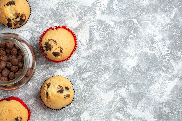 Media foto de deliciosos cupcakes pequeños y chocolate en una olla de vidrio junto al regalo de Navidad en el lado derecho de la mesa de hielo