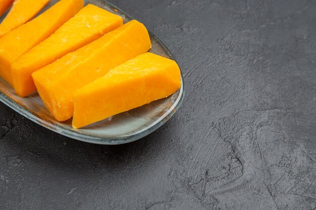 Media foto de queso fresco en rodajas de color amarillo sobre una placa azul en el lado derecho sobre un fondo negro