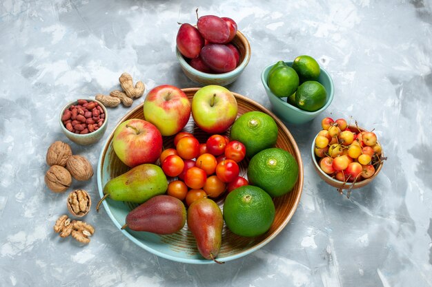 Media vista superior composición de frutas manzanas peras mandarinas y ciruelas en el escritorio blanco.