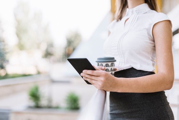 Mediados de sección de una empresaria joven que sostiene el teléfono celular y la taza de café para llevar