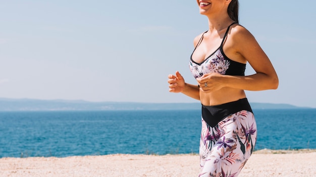 Mediados de sección de jogger de fitness joven corriendo cerca de la playa