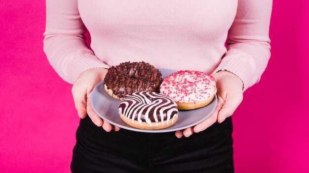 Mediados de sección de una mujer que sostiene la placa de varios donuts sabrosos en la mano contra el fondo rosa