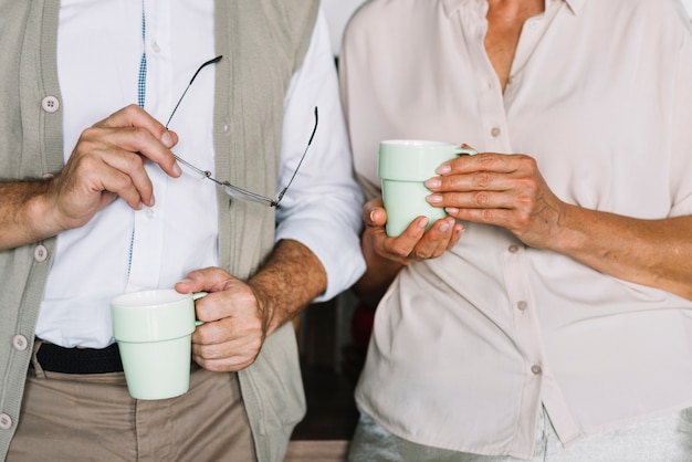 Foto gratuita mediados de sección de una pareja de ancianos sosteniendo la taza de café en la mano