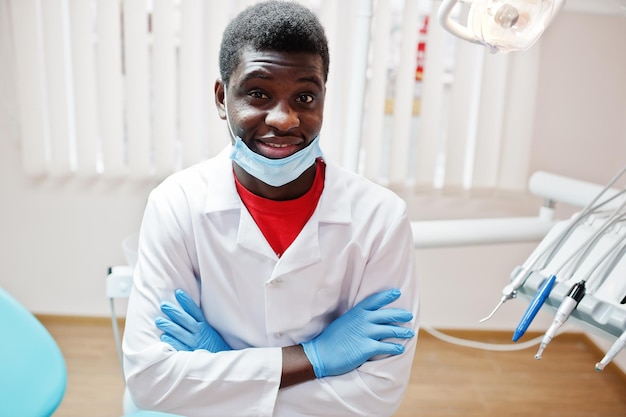 Foto gratuita médico afroamericano enmascarado con brazos cruzados sentado en la silla del dentista en la clínica dental