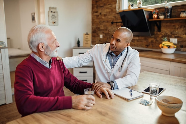 Médico afroamericano hablando con un anciano durante una visita a casa