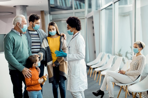 Médico afroamericano hablando con la familia extendida en la clínica médica durante la pandemia del coronavirus