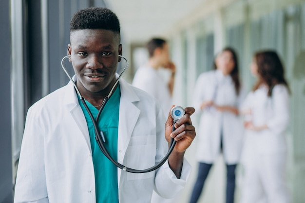 Médico afroamericano hombre con estetoscopio, de pie en el pasillo del hospital