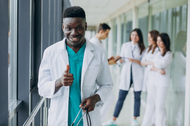 Médico afroamericano hombre con pulgares arriba, de pie en el pasillo del hospital