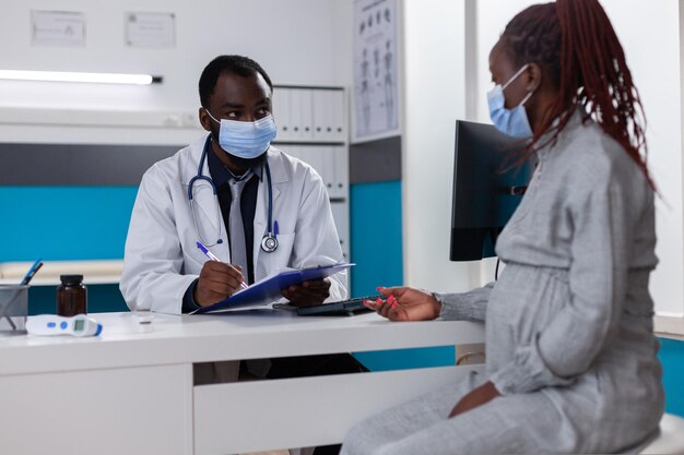 Médico afroamericano y mujer embarazada hablando