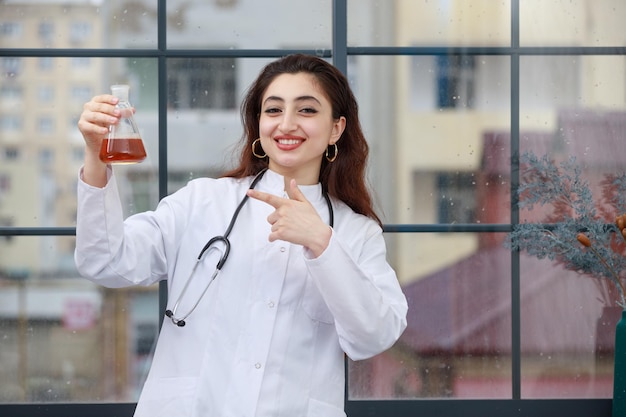 Médico alegre sosteniendo una botella química y señalando con el dedo Foto de alta calidad
