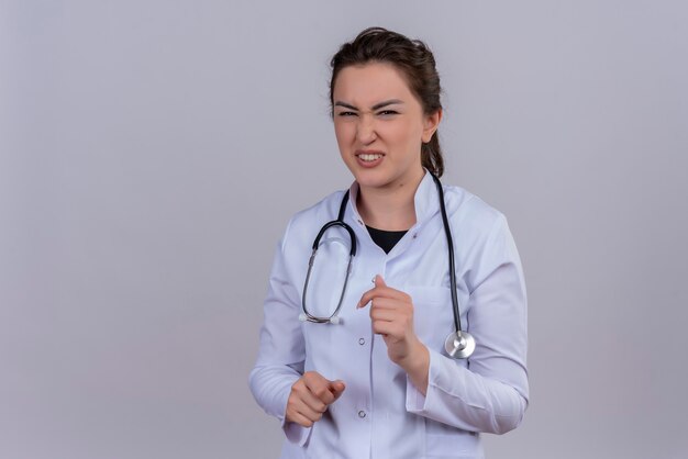 Médico aprensivo joven vistiendo bata médica con estetoscopio sobre fondo blanco