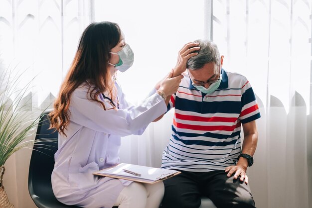 Un médico asiático visita y examina a un anciano en casa con dolor de cabeza El médico revisa y consulta los servicios del hospital de salud para jubilados y usa una máscara para proteger a covid19