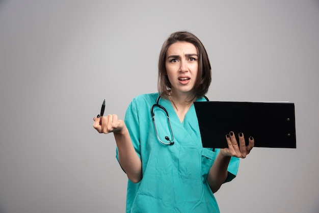 Médico cansado sosteniendo el portapapeles sobre fondo gris. Foto de alta calidad