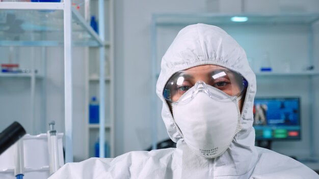 Médico cansado vistiendo un mono mirando agotado a la cámara en el laboratorio equipado moderno. Científico que examina la evolución del virus utilizando herramientas de alta tecnología y química para la investigación científica, el desarrollo de vacunas.