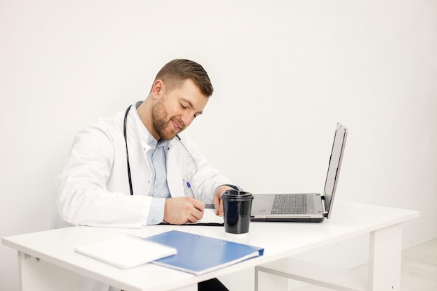 Médico caucásico sentado en el lugar de trabajo y usando una computadora portátil