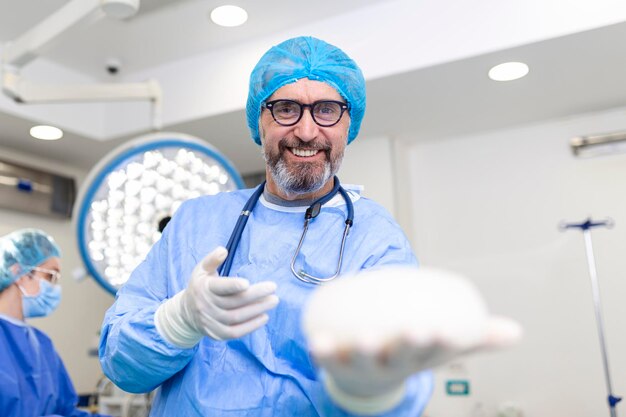 Médico cirujano sonriendo sosteniendo implante mamario de silicona implante mamario en las manos del cirujano