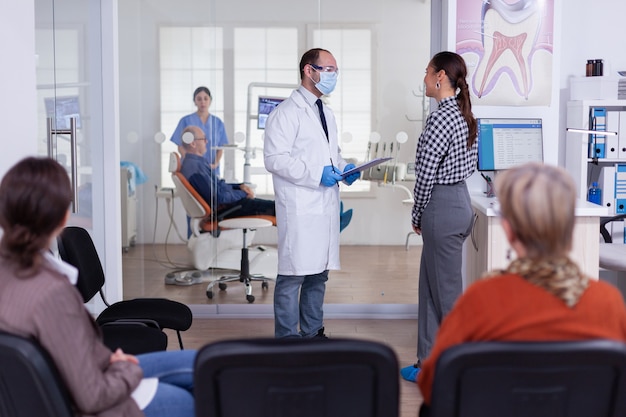 Médico dentista interrogando a la mujer y tomando notas en el portapapeles de pie en la sala de espera