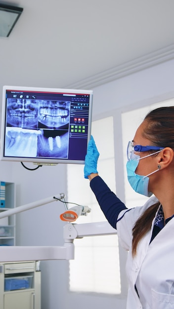 Médico dentista y paciente mirando radiografía digital de dientes en consultorio dental, persona pov. Estomatología con mascarilla protectora y guantes apuntando a la radiografía de los dientes en la clínica estomatológica