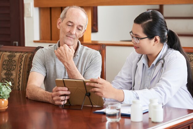 Médico a domicilio que muestra los resultados de la prueba a un paciente anciano en una tableta