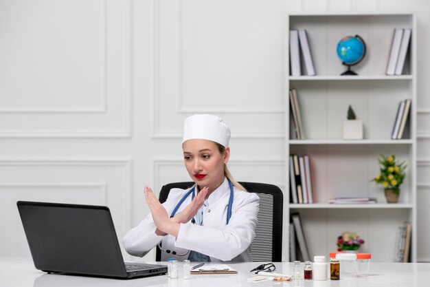 Médico encantador lindo médico en bata de laboratorio blanca y sombrero con computadora que muestra el signo de finalización