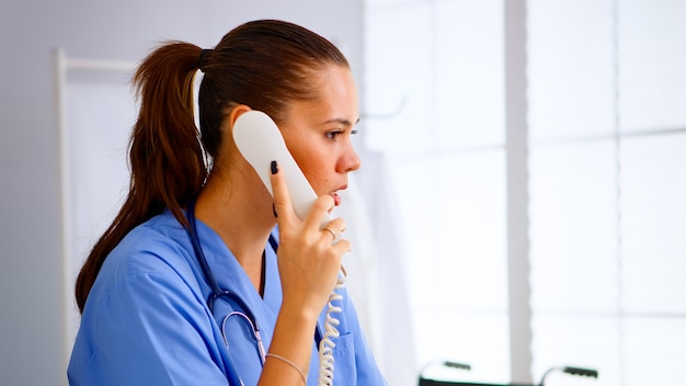 Médico especialista en enfermería que comprueba la cita durante la comunicación de telesalud en el hospital. Médico de atención médica en uniforme de medicina, asistente médico recepcionista que ayuda con la construcción del teléfono