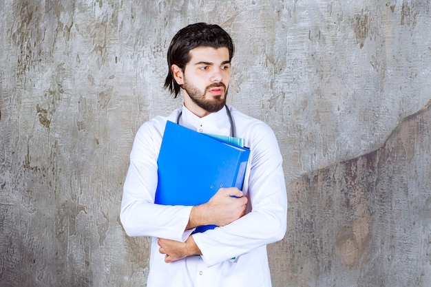 Foto gratuita médico con un estetoscopio sosteniendo varias carpetas de informes de colores y parece confundido o inseguro