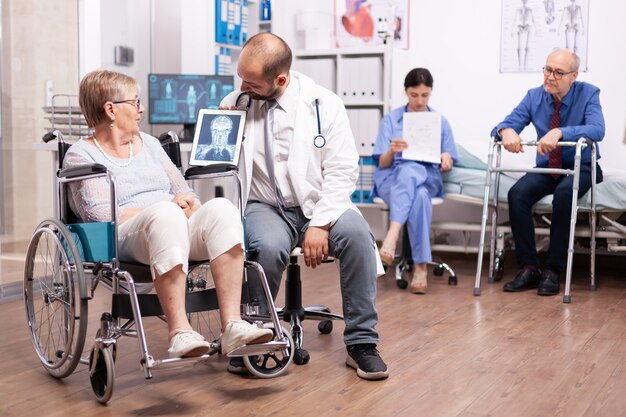 Médico explicando el diagnóstico a la mujer mayor discapacitada en silla de ruedas