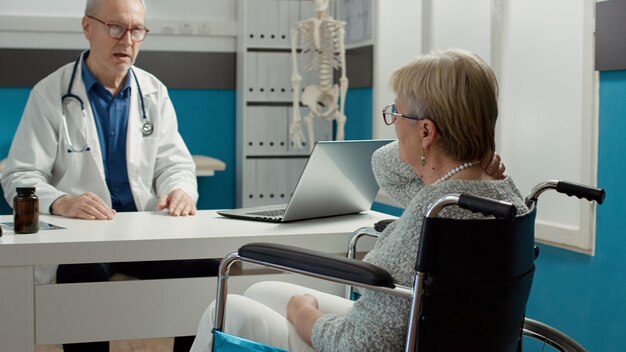 Médico general consultando a una mujer con discapacidad crónica en un consultorio médico, haciendo un examen de control con medicación. Paciente jubilado con deficiencia y condición de salud en la cita.