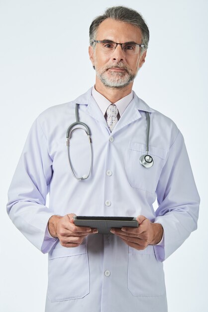 Médico general con estetoscopio sobre los hombros sosteniendo la pestaña digital y mirando a la cámara
