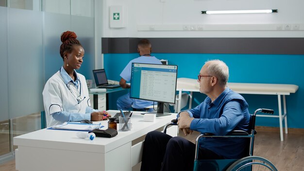 Médico general haciendo una visita de control con un paciente en silla de ruedas, consultando a un anciano con discapacidad crónica. Médico haciendo un examen con un usuario de silla de ruedas que sufre de discapacidad.