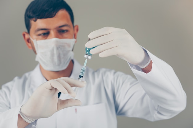 Médico con guantes y máscara rellenando la jeringa en un vial. vista lateral horizontal