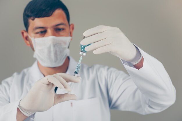 Médico con guantes y máscara rellenando la jeringa en un vial. vista lateral horizontal