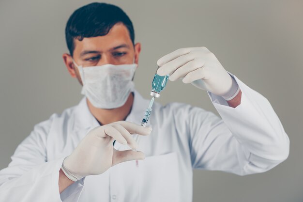 Médico con guantes y máscara rellenando la jeringa en un vial. vista lateral horizontal