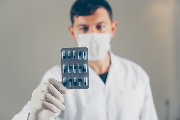 Médico con guantes y máscara sosteniendo una vista lateral del paquete de píldoras