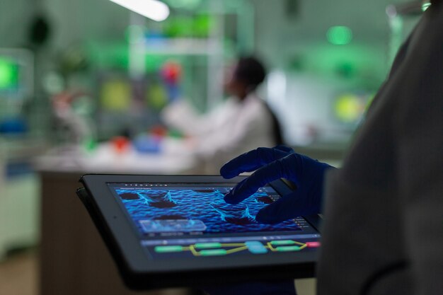 Médico investigador científico que analiza la prueba de mutación genética con tableta mientras su colega escribiendo conocimientos biológicos en la computadora
