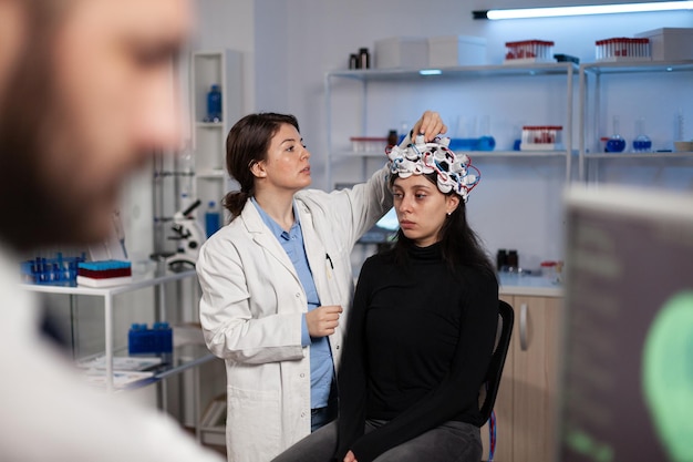 Médico investigador neurólogo ajustando el escáner eeg en la cabeza del paciente analizando la evolución del cerebro trabajando en el diagnóstico de enfermedades durante el experimento de neurología en el laboratorio de alta tecnología. Doctor explicando la tomografía