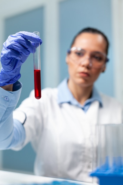 Médico investigador sosteniendo un tubo de ensayo transparente con sangre trabajando en el experimento de bioquímica