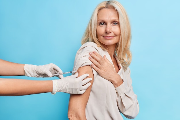 Foto gratuita médico irreconocible con guantes médicos sostiene una jeringa que inyecta la vacuna a una paciente de mediana edad