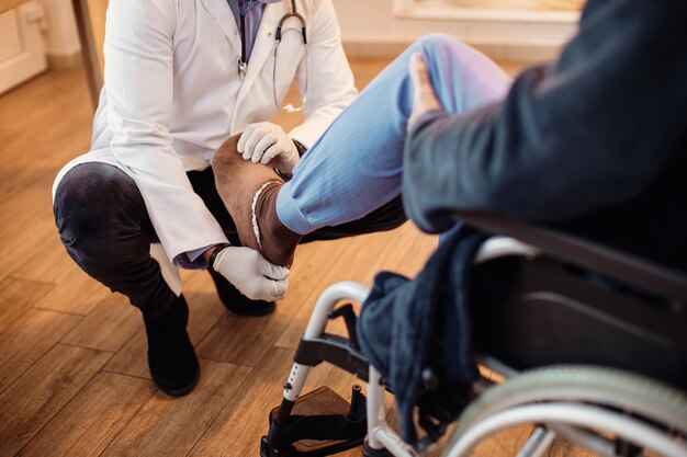 Médico irreconocible que examina la pierna de un paciente mayor en un hogar de ancianos