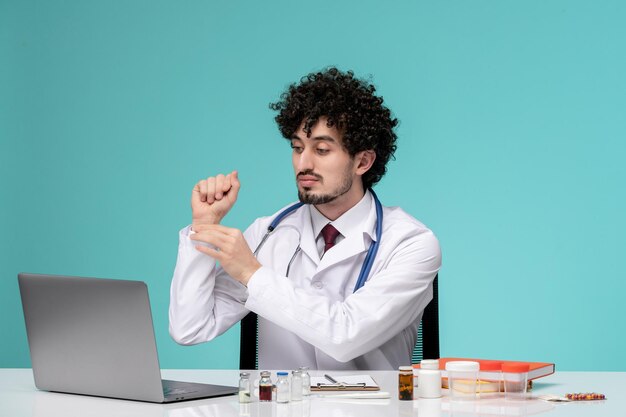 Médico joven apuesto médico que trabaja en la computadora de forma remota en bata de laboratorio comprobando el pulso