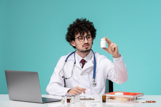 Médico joven y apuesto que trabaja en una computadora de forma remota en bata de laboratorio mirando medicamentos